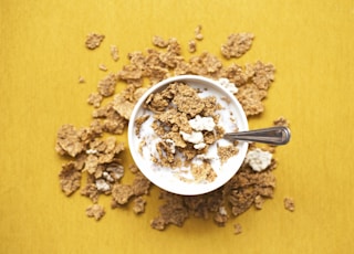 top view of corn flakes in bowl with milk and silver spoon