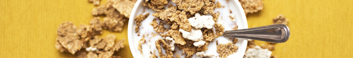 top view of corn flakes in bowl with milk and silver spoon