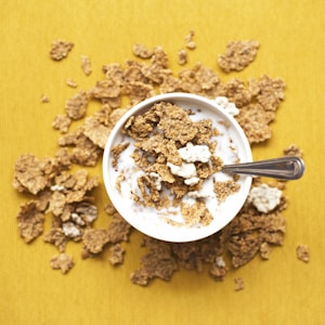 top view of corn flakes in bowl with milk and silver spoon