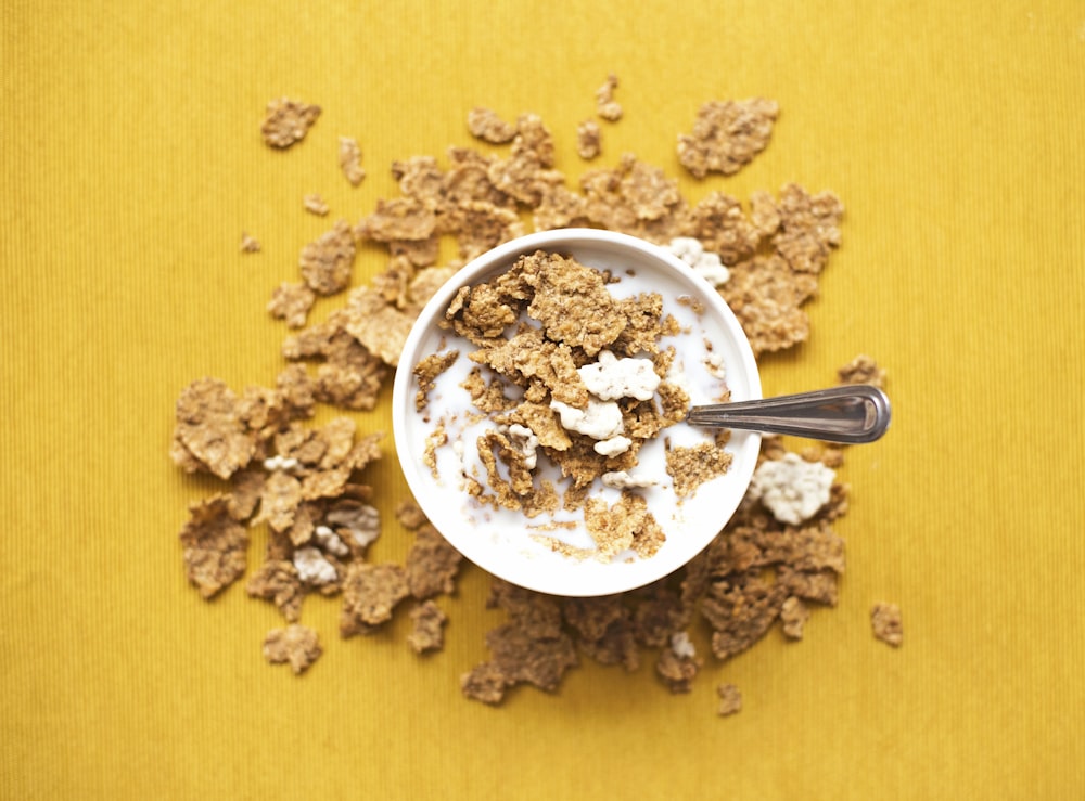 top view of corn flakes in bowl with milk and silver spoon