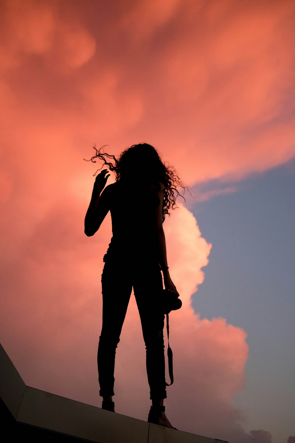 silhouette of woman standing under orange sky during sunset