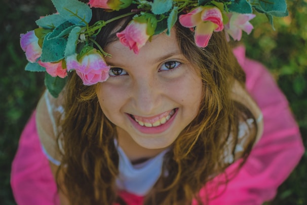 A joyful 15-year-old girl smiling brightly in a sunlit garden, wearing a delicate floral crown.