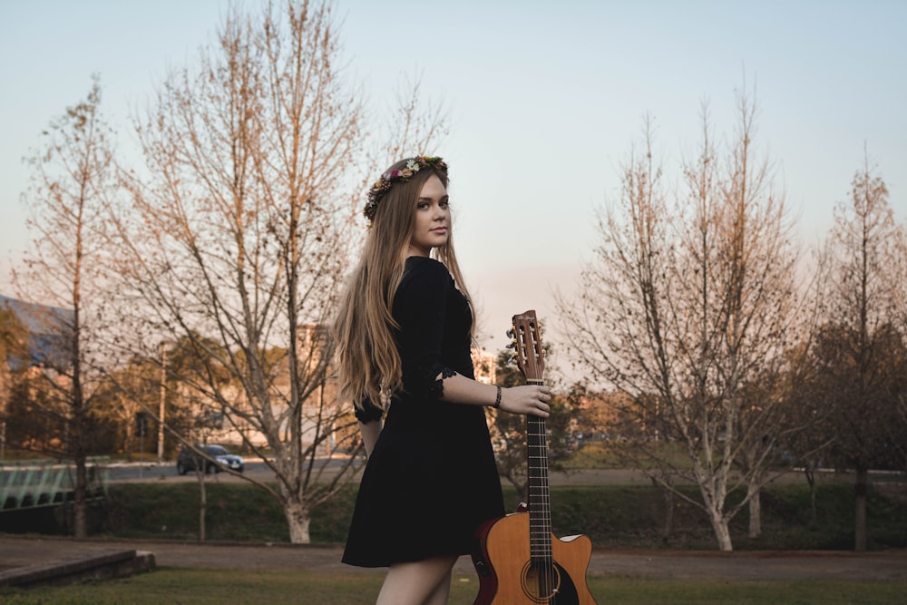 woman standing on lawn while holding classical guitar