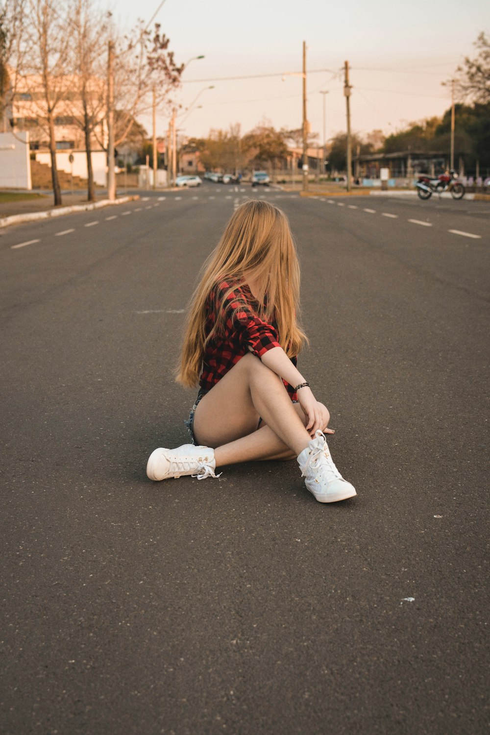 Donna in camicia a quadretti nera e rossa che si siede sulla strada durante il giorno