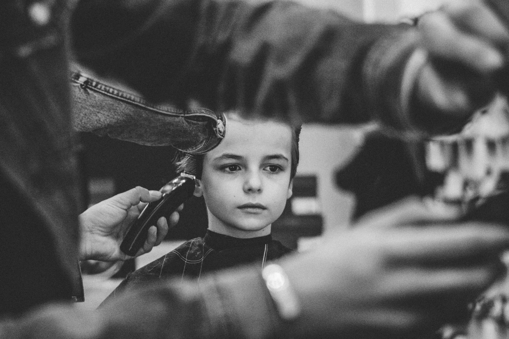 A boy sitting in a barber chair having his hair combed and trimmed.