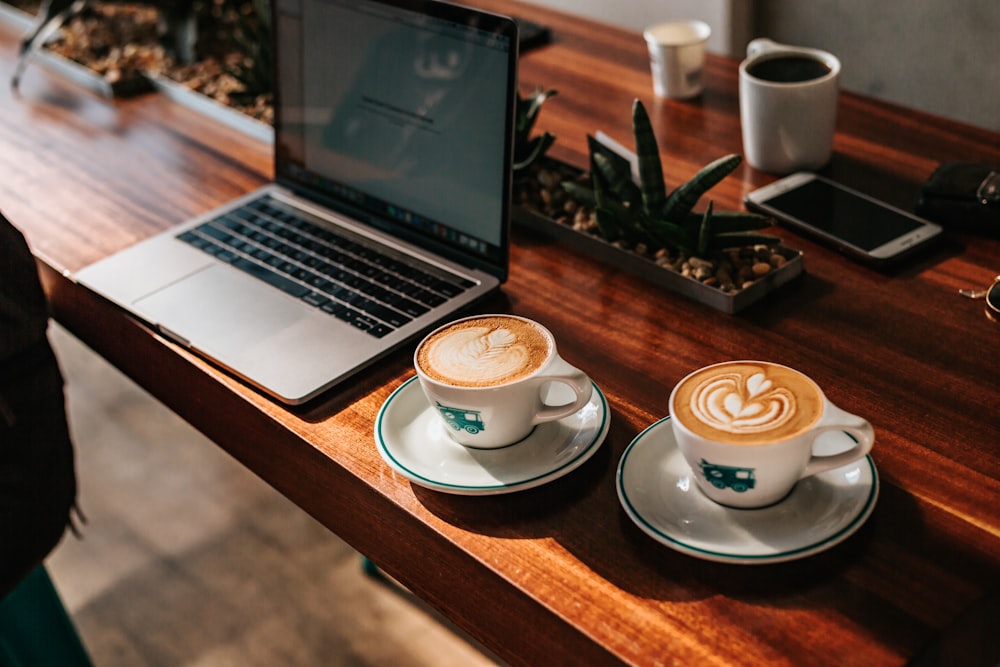 Zwei Cappuccino, die auf Tassen in der Nähe des Laptops serviert werden
