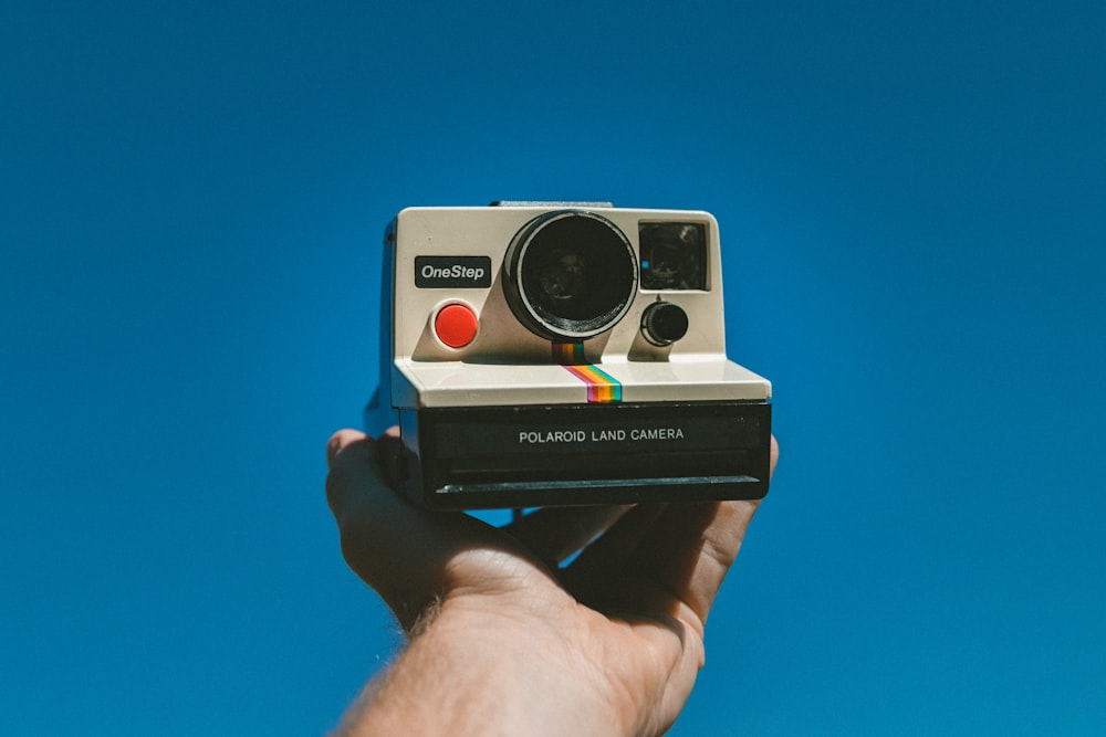 person holding up white and black Polaroid One Step instant printing camera in left hand