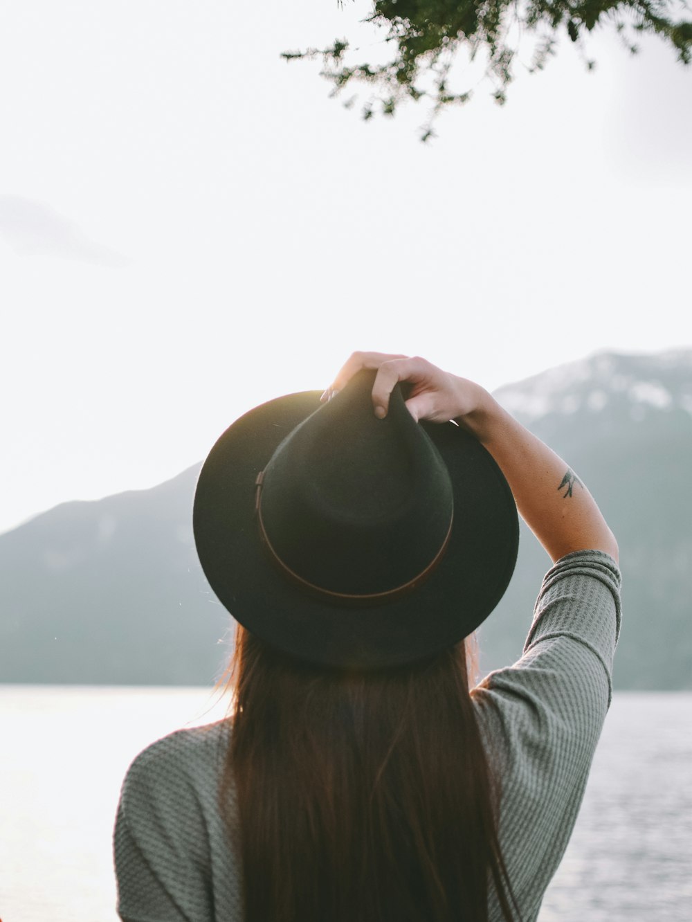 Donna che indossa il cappello Fedora nero vicino allo specchio d'acqua durante il giorno