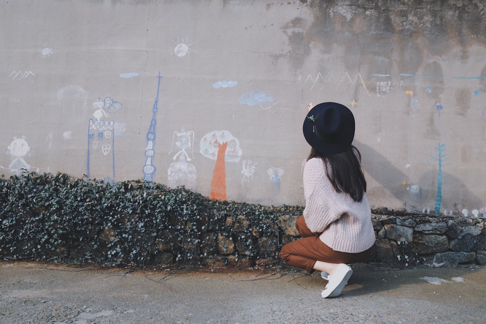 woman kneeling near gray concrete wall with full of drawings