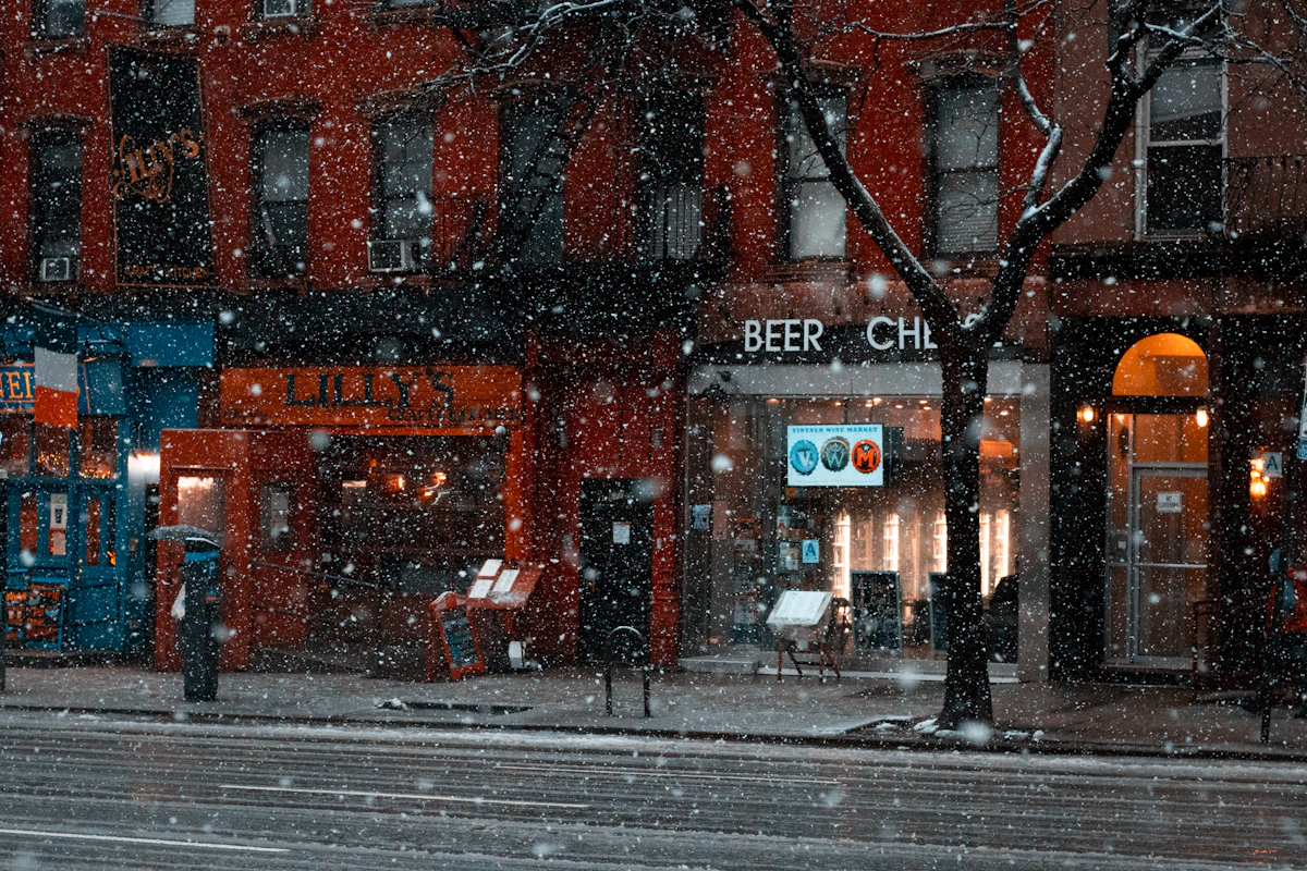 Row of lit shop fronts on a New York street during a snowfall