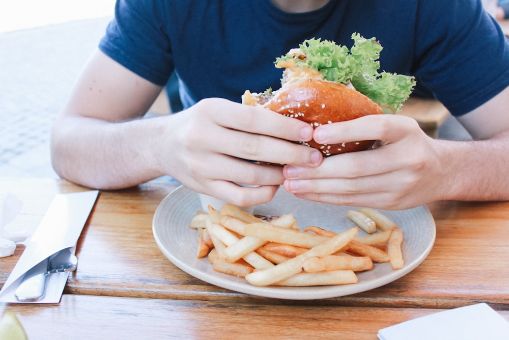 personne mangeant un hamburger avec des frites dans une assiette