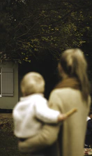 shallow focus photography of woman carrying baby in front of house