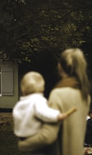 shallow focus photography of woman carrying baby in front of house