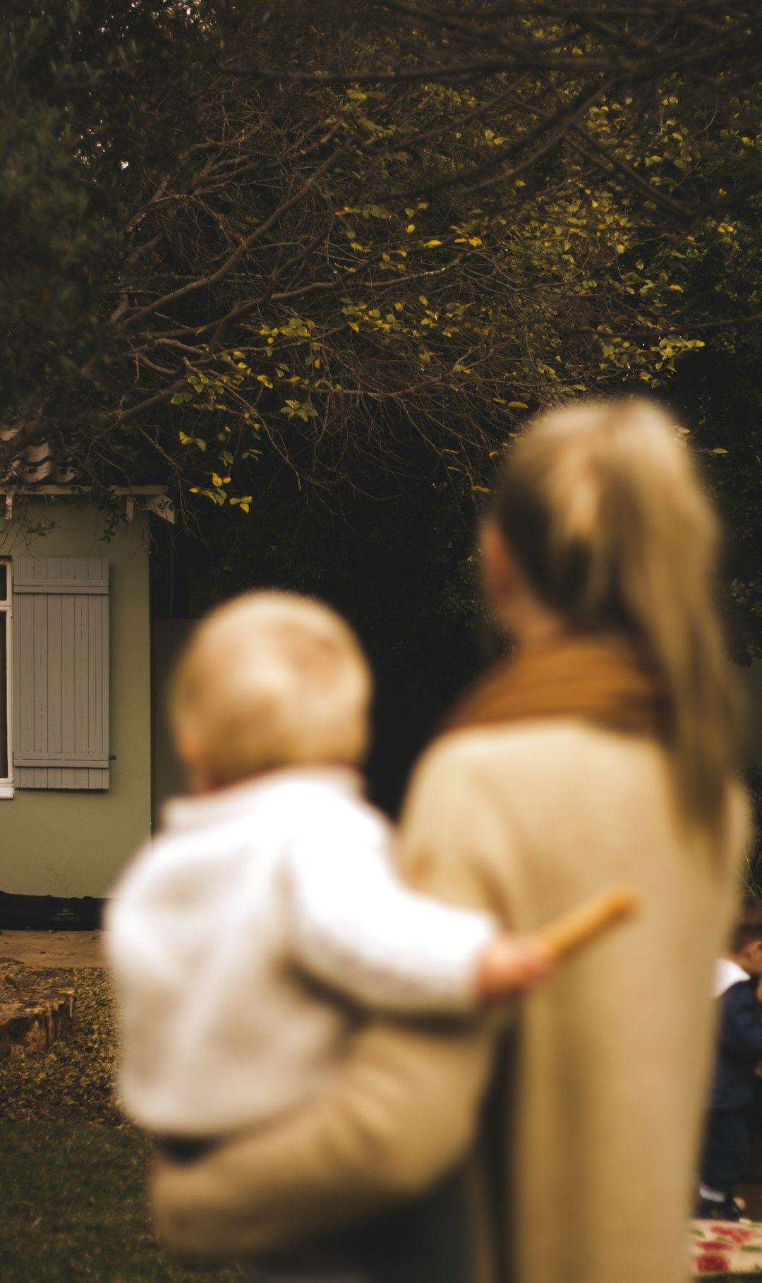 shallow focus photography of woman carrying baby in front of house