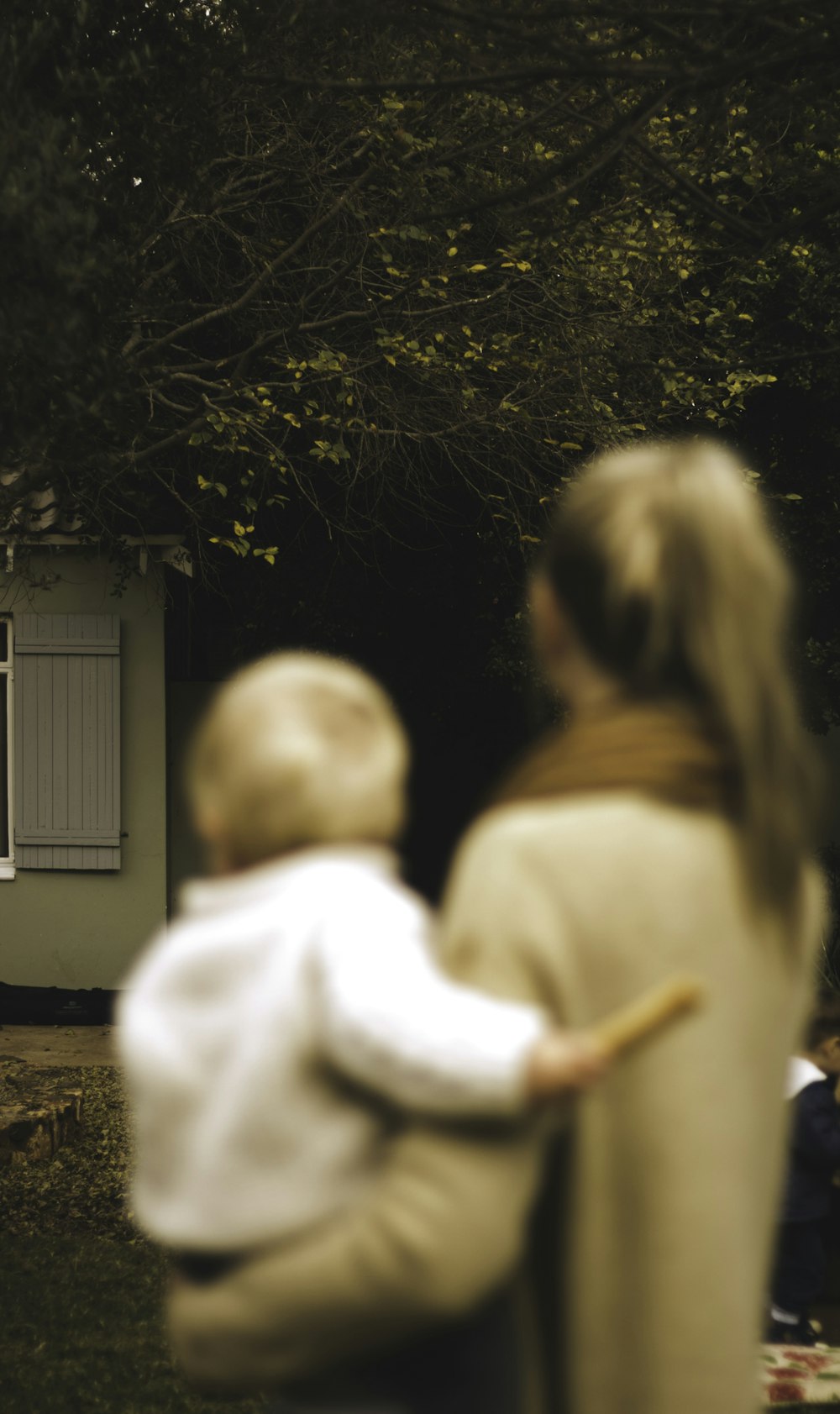 shallow focus photography of woman carrying baby in front of house