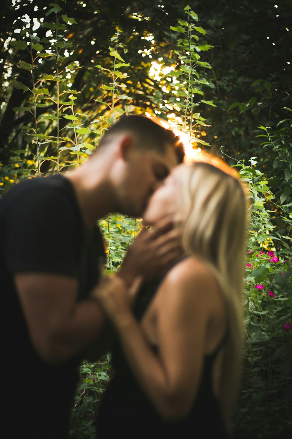 Homem e mulher se beijando sob árvores verdes durante o dia