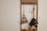 A minimalistic wall-mounted organizer holding two cleaning tools, a dustpan with a brush and a feather duster. The objects are hanging against a plain wall with a light switch nearby, framed by a simple wooden structure.