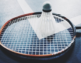 white shuttlecock on brown and black badminton racket placed on floor