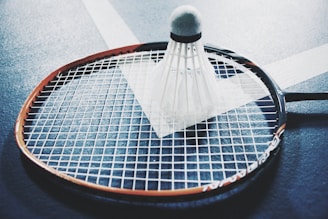 white shuttlecock on brown and black badminton racket placed on floor