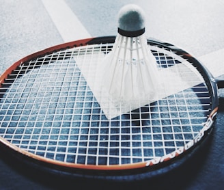 white shuttlecock on brown and black badminton racket placed on floor