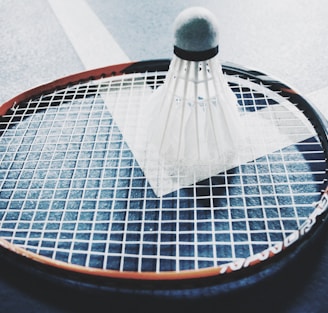 white shuttlecock on brown and black badminton racket placed on floor