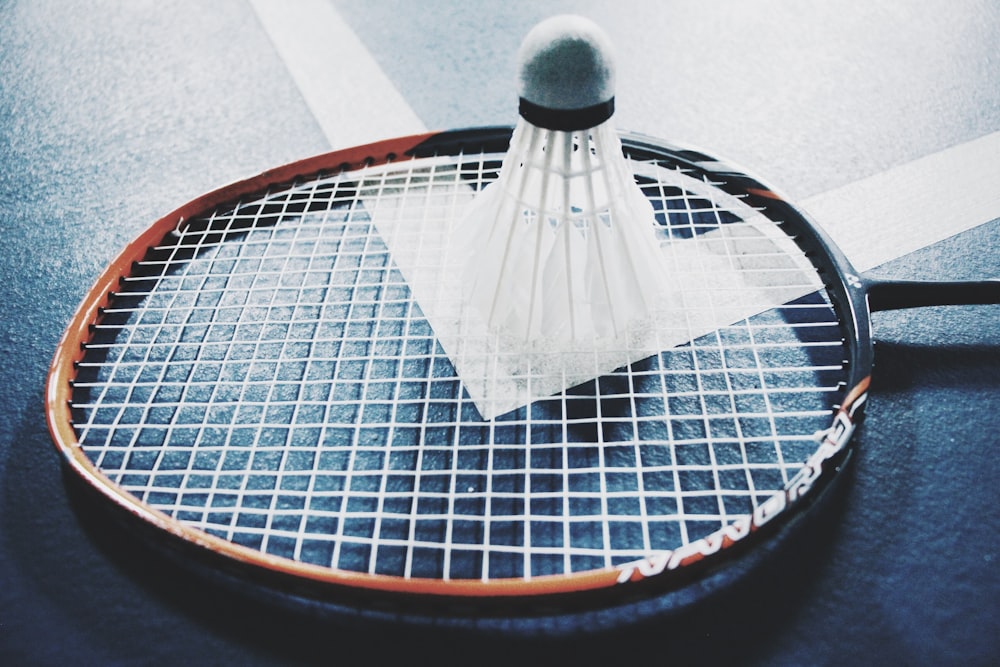 weißer Federball auf braunem und schwarzem Badmintonschläger auf dem Boden