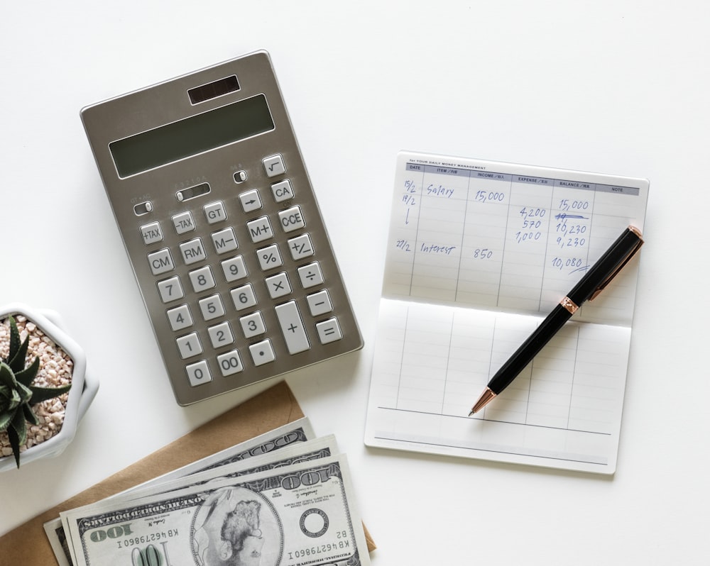 flatlay photography of calculator between stack of banknote and click pen