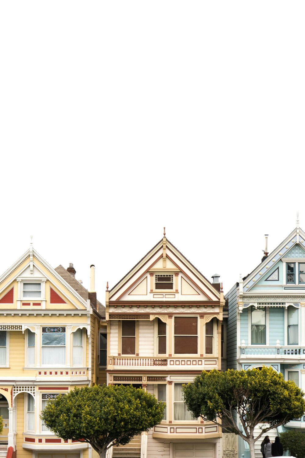 Trois maisons aux couleurs variées sous des nuages blancs