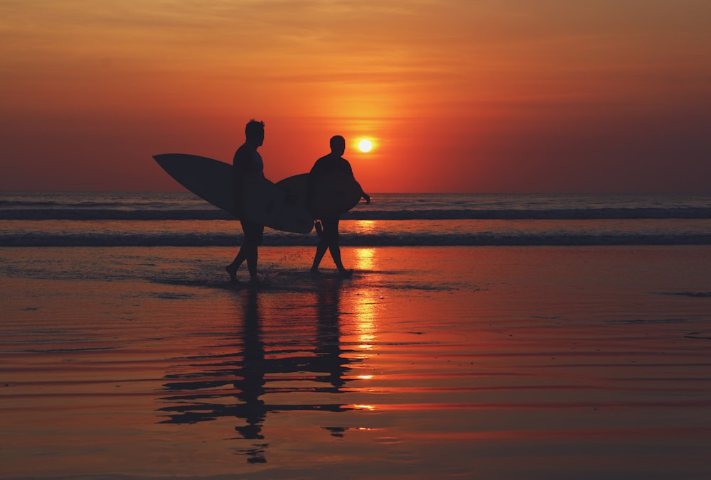 silhouette of two people walking on seashore during sunset