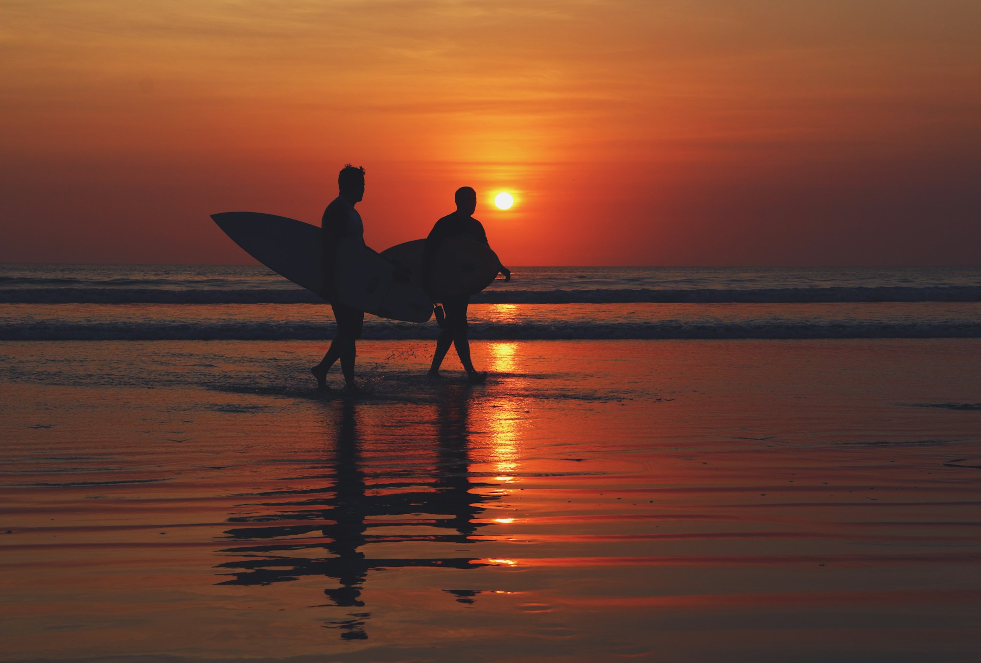 silhouette of two people walking on seashore during sunset