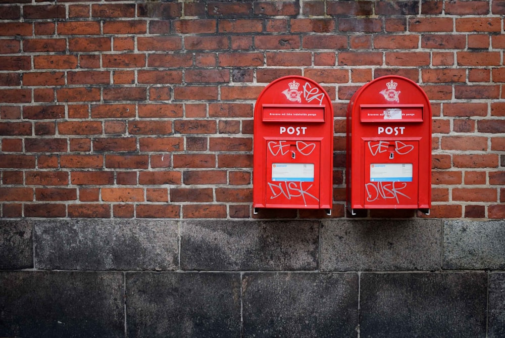 茶色のコンクリートの壁に取り付けられた2つの赤い郵便ポストの写真