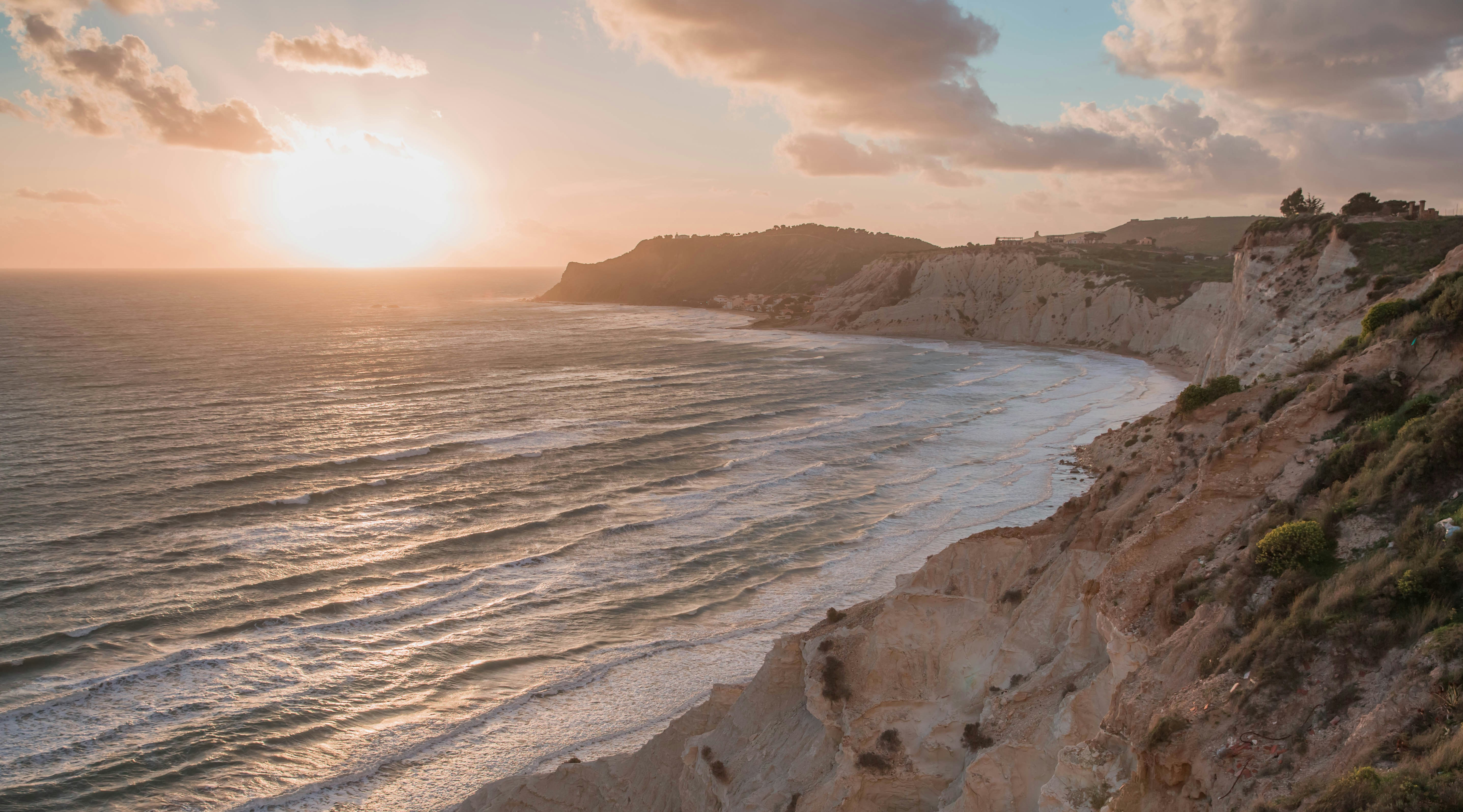 Algarve golden cliffs at sunset, dramatic orange rock formations, dark Atlantic ocean, cinematic low sun, shadowed foreground
