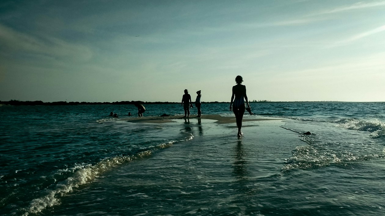 Personas caminando sobre un banco de arena en agua de mar muy baja al final de la tarde