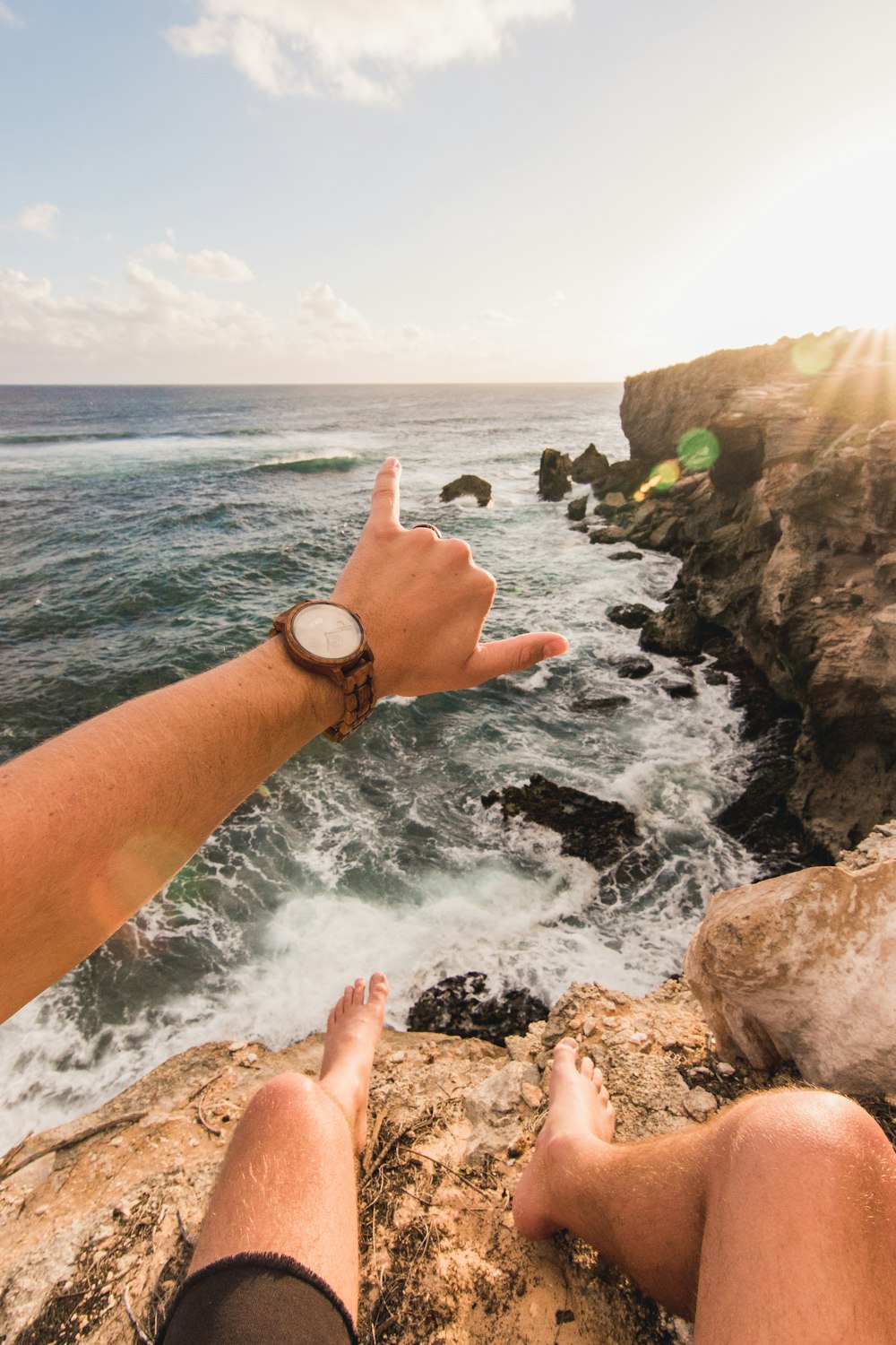 man sitting on cliff facing body of water