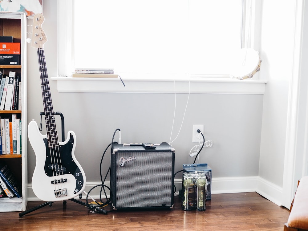 guitarra stratocaster blanca y negra sobre soporte de guitarra negro junto al amplificador de guitarra Fender negro