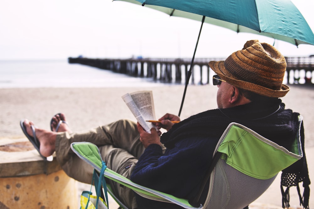 homme assis sur une chaise avec un parapluie vert