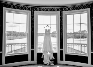grayscale photo of gown hanged on window
