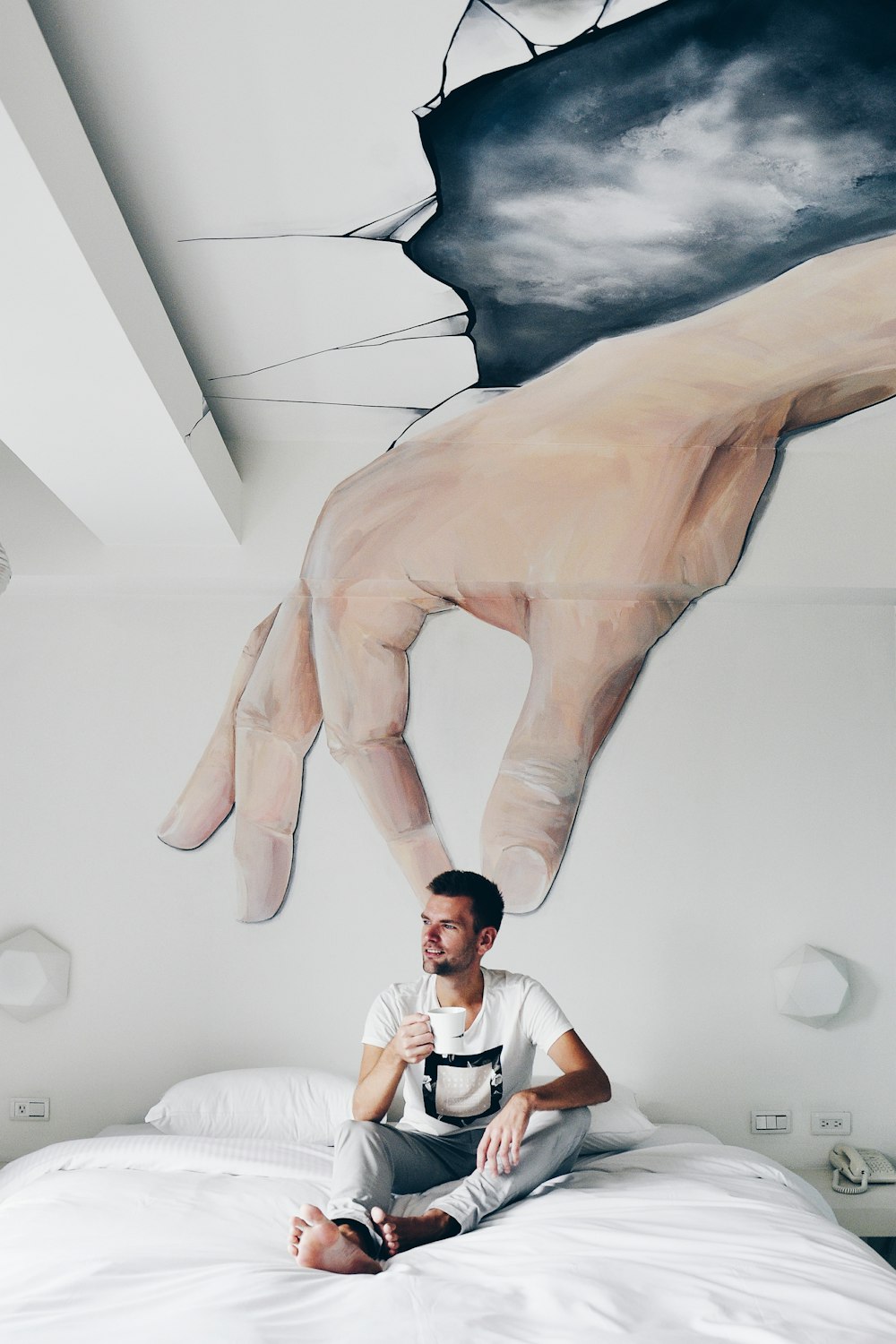 man sitting on bed while holding ceramic mug