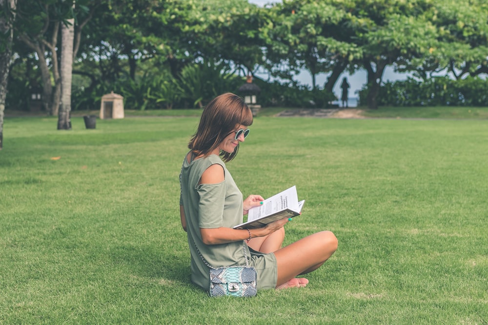mulher sentada na grama verde enquanto lê o livro