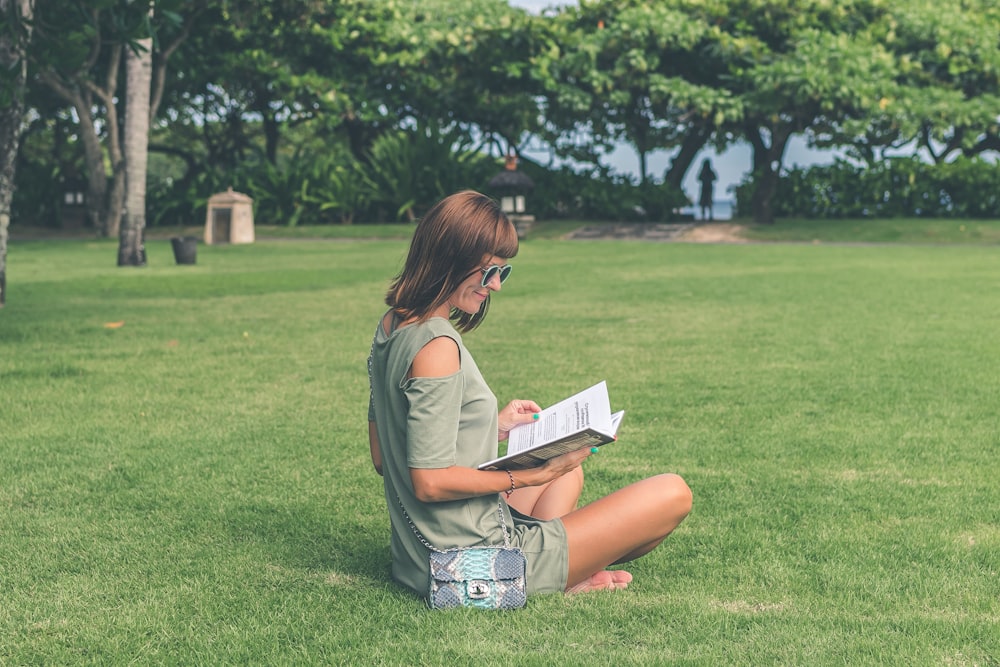 woman sitting on green grass while reading book