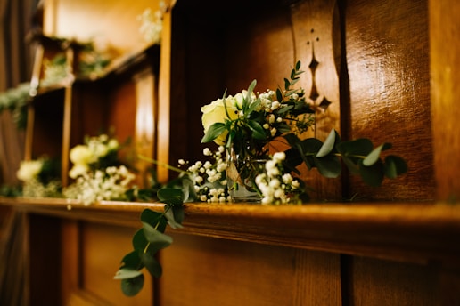 A wooden shelf decorated with small vases containing greenery and yellow flowers, including delicate white blossoms, arranged in a rustic and natural style.