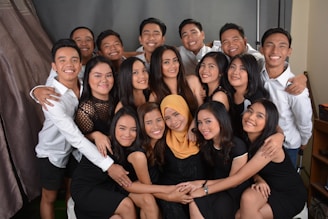 A group of smiling people are closely gathered, dressed in black and white attire. Several individuals are wearing black dresses, while others wear white shirts. They appear to be posing for a group photo, exuding a sense of camaraderie.