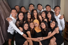 A group of smiling people are closely gathered, dressed in black and white attire. Several individuals are wearing black dresses, while others wear white shirts. They appear to be posing for a group photo, exuding a sense of camaraderie.