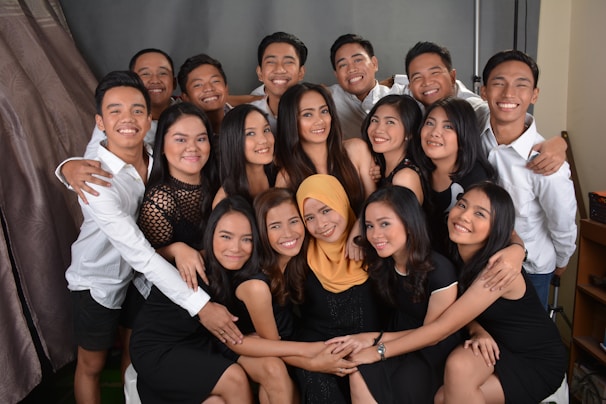 A group of smiling people are closely gathered, dressed in black and white attire. Several individuals are wearing black dresses, while others wear white shirts. They appear to be posing for a group photo, exuding a sense of camaraderie.