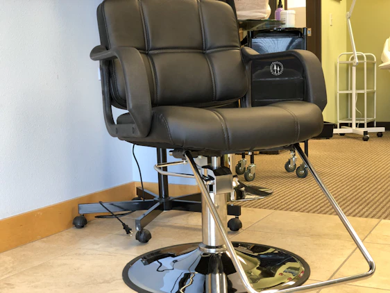 A sleek, matte black barber chair illuminated by soft silver lighting in a minimalist, modern studio setting.