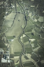 An aerial view of an agricultural landscape featuring numerous fields of varying sizes and shapes, bordered by a winding river. Small clusters of buildings or houses are scattered throughout the area, along with a network of roads connecting them.