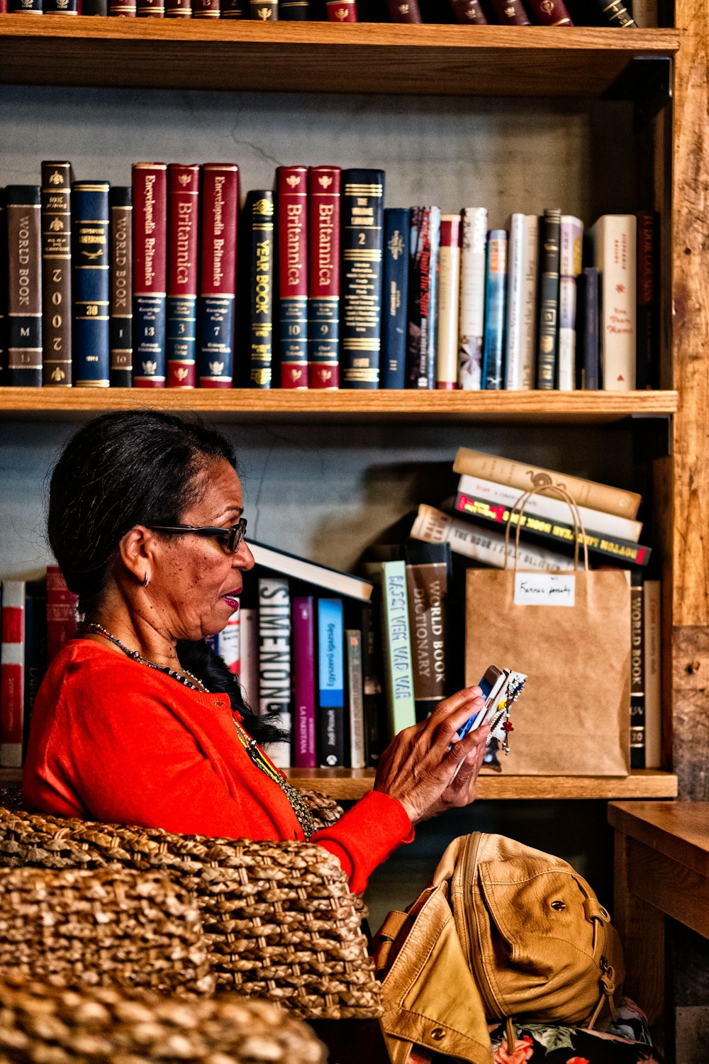 Frau sitzt auf Stuhl mit Android-Smartphone in der Nähe des Bücherregals