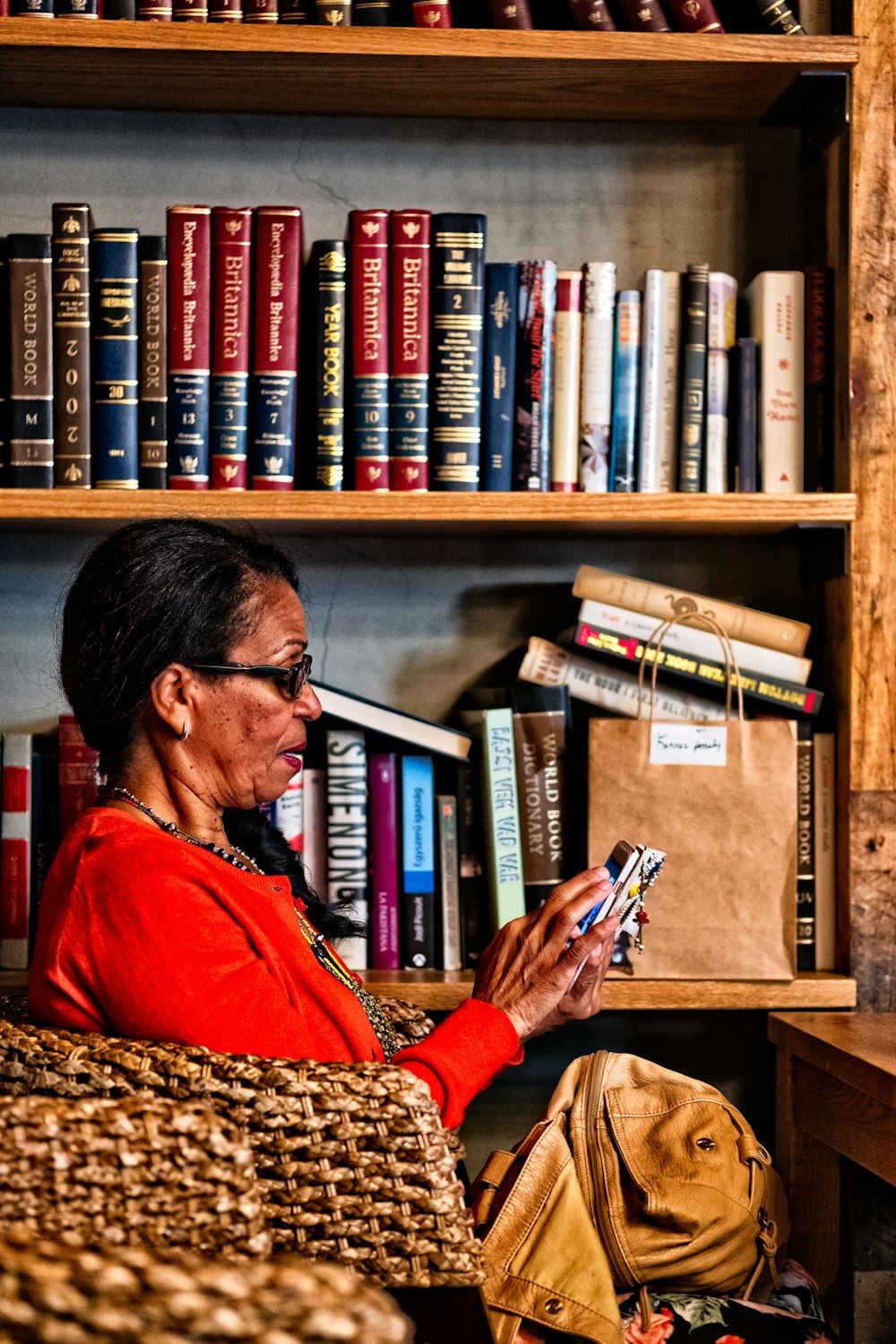 woman sitting on chair using Android smartphone near bookshelf