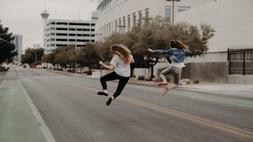 two woman jumping on the street during daytime
