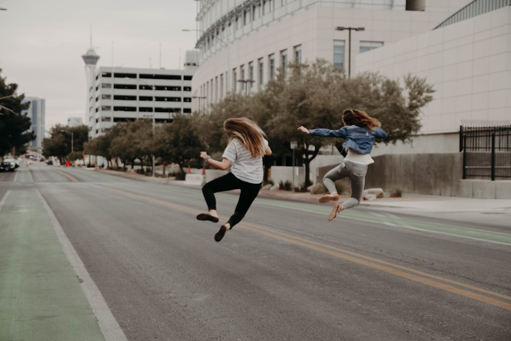 two woman jumping on the street during daytime